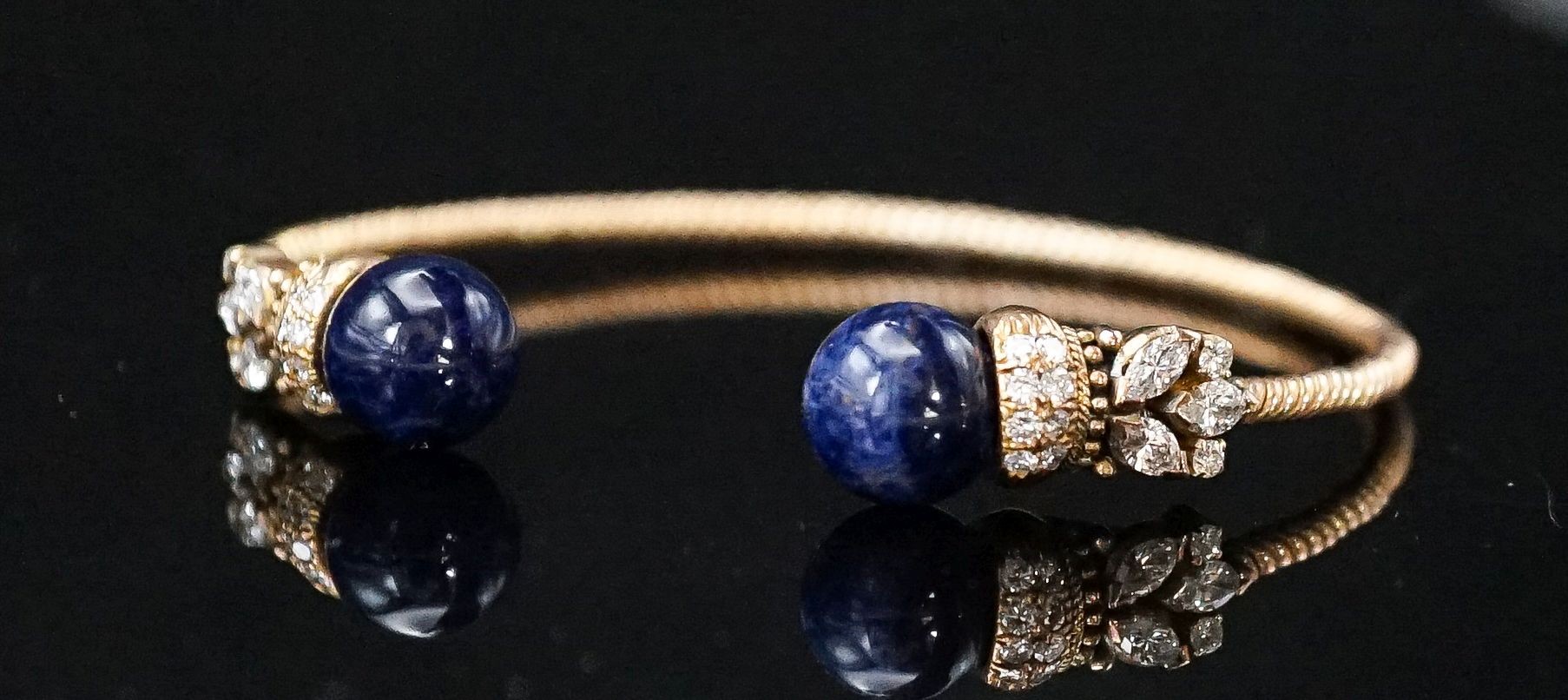 A modern yellow metal twist, two stone sodalite? and diamond set open bangle, gross weight 14 grams.